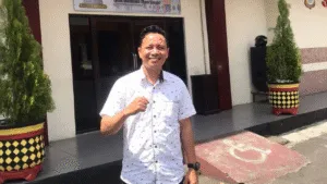 Potret Alwalid Muhammad berdiri memberikan mengepalkan tangan sebagai simbol perjuangan dalam advokasi kemanusiaan, mengenakan kemeja rapi dengan ekspresi penuh keteguhan dan kepemimpinan.