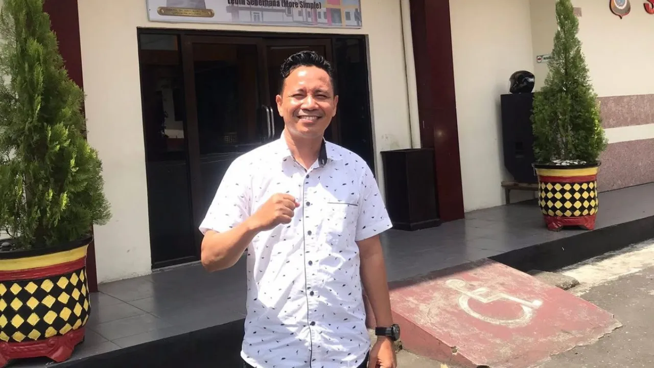 Potret Alwalid Muhammad berdiri memberikan mengepalkan tangan sebagai simbol perjuangan dalam advokasi kemanusiaan, mengenakan kemeja rapi dengan ekspresi penuh keteguhan dan kepemimpinan.