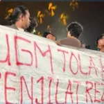 Massa aksi membentangkan spanduk berisi kritik tajam dan penolakan terhadap Budiman Sudjatmiko serta Nusron Wahid di tengah forum diskusi "Pancasila Pemersatu Bangsa" di GIK UGM, Yogyakarta, Senin (15/6/2026). Ketegangan ini memaksa panitia dan aparat keamanan mengevakuasi para pejabat negara tersebut dari lokasi acara. (Foto: Istimewa)